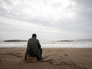 Ein Mann sitzt auf einer Kiste alleine am Strand.