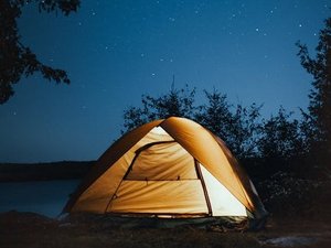 Beleuchtetes Campingzelt in der Natur unter einem Sternenhimmel.