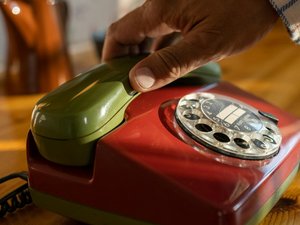 Die Hand einer älteren Person greift nach einem Telefonhörer.